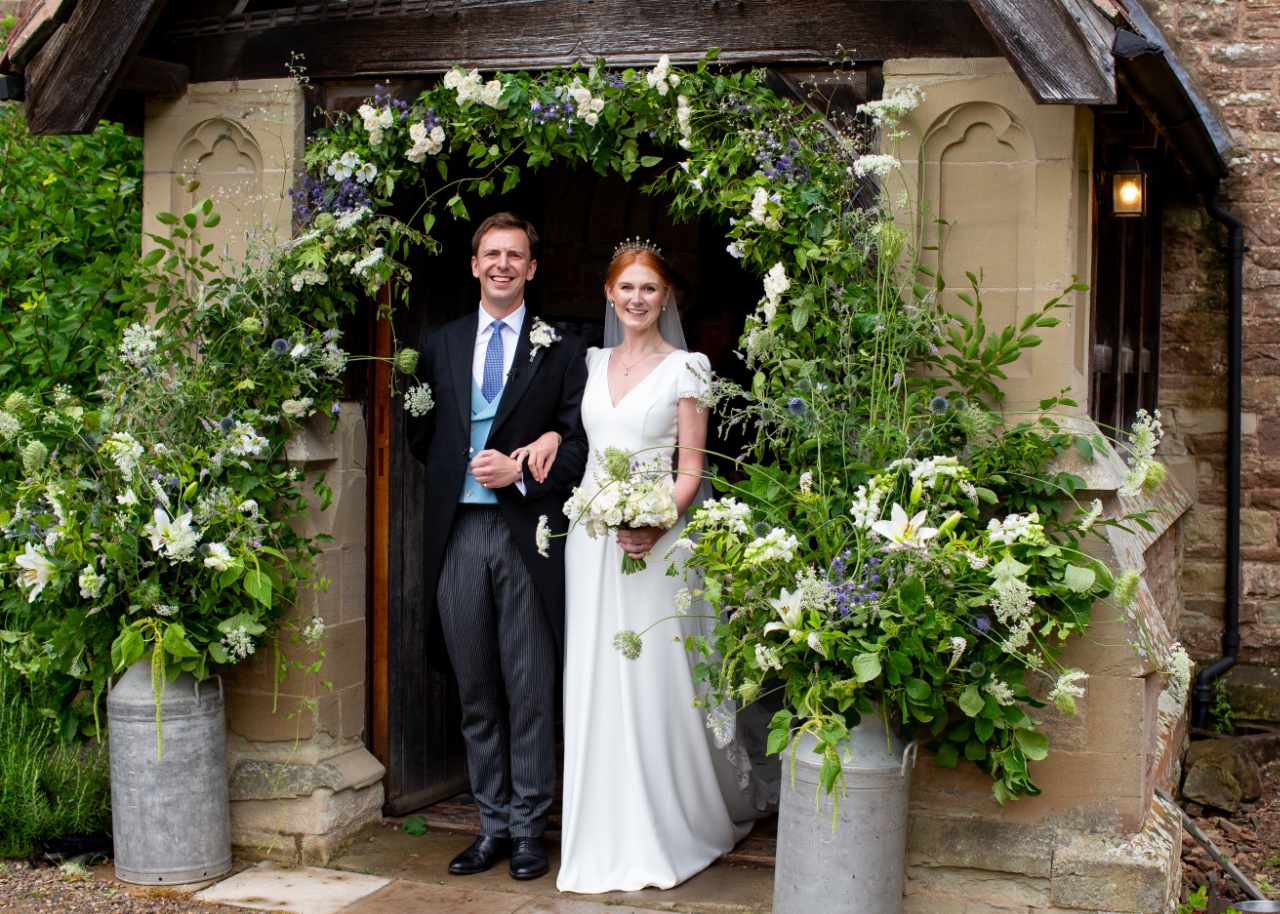 Bride and groom outside church surrounded by floral archway and urns of flowers