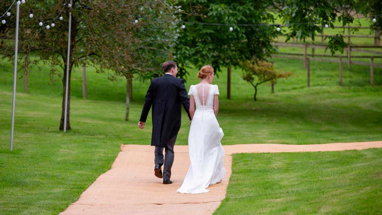 Bride and groom walking down pathway of field